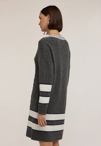 Abito grigio a maglia con maniche lunghe. Presenta strisce bianche e blu navy sulle maniche e sull'orlo. Finitura testurizzata, scollatura tonda, lunghezza al ginocchio.