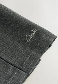 Grått tyg med en texturerad väv, med en vikt fåll och en broderad "Clarks"-logotyp i ljusgrå tråd.