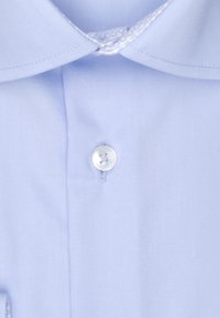 Maglietta azzurra chiara con colletto a punta, chiusura con un bottone rotondo singolo e una texture di tessuto liscia con dettagli di cucitura sottili.