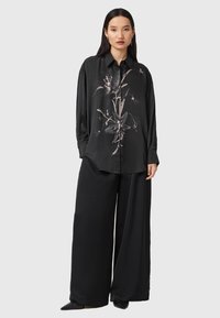 Chemise noire en satin à manches longues avec un imprimé floral. Associée à un pantalon noir à jambes larges, offrant une coupe décontractée et une texture lisse.