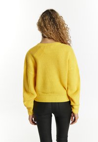 Gelber gestrickter Pullover mit lockerer Passform, weiten Ärmeln und geripptem Saum. Glatte Textur, lässiges Design, von hinten gesehen.