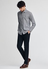 Grå rutig skjorta med knappar, långa ärmar. Kombinerad med svarta byxor och bruna snörskor. Enkel design och figurnära silhuett.