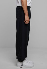 Sorte, løstsiddende sweatpants med en sidelomme, elastiske ankler og snoretræk. Kombineret med hvide sneakers.