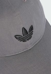 Siva baseball kapa napravljena od teksturirane tkanine s zakrivljenim vizirjem. Sadrži crni izvezeni logo sprijeda.