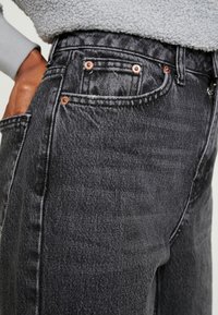 Černé džíny s vysokým pasem, s měděnými nýty, předními kapsami a mírně vybledlou texturou.