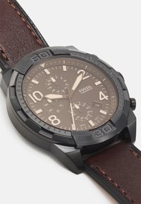 Dunkelbraune Chronographuhr mit einem schwarzen Edelstahlgehäuse, strukturiertem Ring und Lederarmband. Verfügt über große Ziffern und Unterzifferblätter.