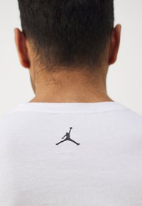 Fehér pamut póló, hátul fekete Jumpman logóval, klasszikus kerek nyakkal és puha textúrával.