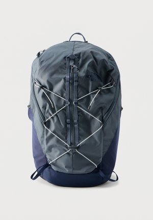 Sac à dos gris foncé et bleu marine avec cordon élastique à l'avant, poche zippée verticale, poignée supérieure et logo sur le côté supérieur droit.