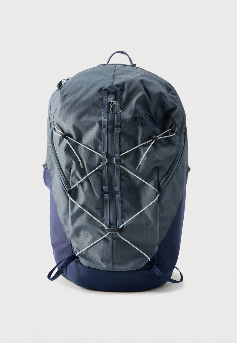 Tummanharmaa ja tummansininen reppu, jossa etuosassa joustava naru, pystysuora vetoketjutasku, yläkahva ja logo oikeassa yläkulmassa.