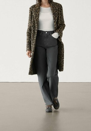 Personne portant un long manteau à imprimé léopard, un haut blanc, un pantalon taille haute gris foncé et des chaussures grises à lacets marchant vers l'avant.