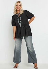 Top peplum nero con maniche a sbuffo corte e scollatura annodata caratterizzata da nastri a motivo bianco e nero, abbinato a jeans a gamba larga grigio chiaro.