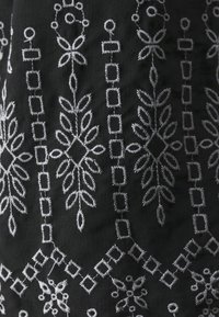 Tissu noir avec une broderie blanche délicate présentant des rangées verticales de motifs géométriques et floraux.