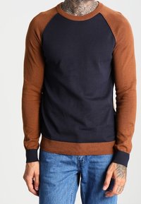 Suéter de bloques de color con cuerpo azul marino y mangas raglán marrones. Fabricado en un tejido suave con puños y dobladillo acanalados. Ajuste casual.