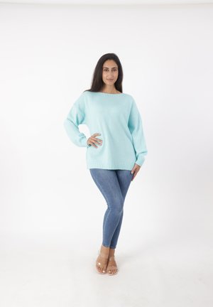Maglione azzurro chiaro a maglia con vestibilità comoda e orlo a costine, abbinato a jeans blu attillati e sandali trasparenti con cinturini.
