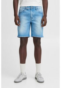 Shorts en denim bleu clair avec une coupe droite, ourlet brut, deux poches avant et fermeture à bouton. Associés à des baskets grises et des chaussettes blanches.