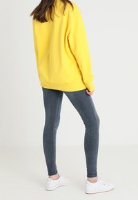 Yellow sweatshirt with long sleeves and ribbed cuffs, paired with fitted dark grey leggings and white sneakers, showcasing a casual outfit.