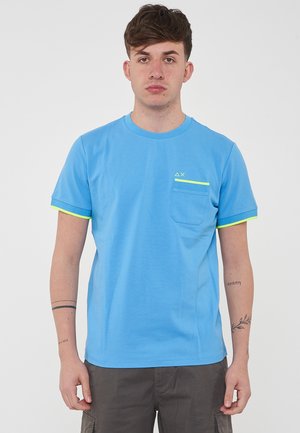 T-shirt di cotone blu chiaro con maniche corte, rifiniture in giallo neon sui bordi delle maniche e sulla tasca, con un piccolo logo sul petto.