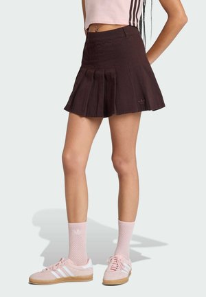 Bruine geplooide rok met een A-lijnvorm, gemaakt van stof, gecombineerd met roze schoenen en sokken, voorzien van subtiele branding en textuurlijke details.