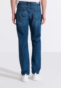 Jeans in denim blu sbiadito dal taglio dritto, design a cinque tasche e etichetta in pelle marrone nella parte posteriore della vita. Indossati con sneakers bianche.