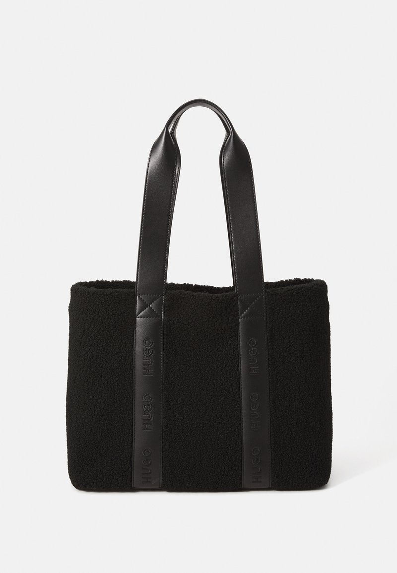 Saco tote preto com um corpo de pelúcia texturizada e alças de couro liso. Apresenta uma marcação em relevo nas alças e tem um formato retangular.