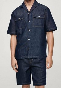 Zestaw z ciemnego denimu: koszula i szorty. Krótkie rękawy, zapięcie na guziki z przodu, dwie kieszenie na piersi. Charakteryzuje się kontrastowymi szwami i luźnym krojem.