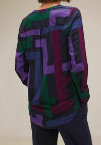 Långärmad skjorta med ett geometriskt mönster i lila, grönt och svart. Tyget har en subtil textur och en rundad nederkant.