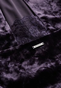 Lilla fløjlstof med en glat tekstur og blonde detaljer. Har et sølv hardwaremærke med "SUPERDRY" indgraveret.