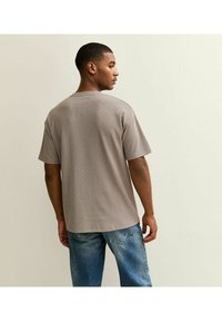 T-shirt light brown a vestibilità rilassata, con maniche corte, texture a coste e scollatura rotonda. Abbinato a jeans in denim blu.