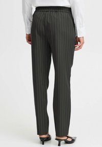 Donkergroene gestreepte broek met een elastische tailleband, recht gesneden en een gladde textuur. Gecombineerd met zwarte hoge hakken.