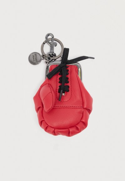 Μπρελόκ από κόκκινο δέρμα σε σχήμα γαντιού του μποξ με μαύρη δαντέλα και στρογγυλό μεταλλικό ταμπελάκι προσαρτημένο σε μεταλλικό κρίκο κλειδιών.