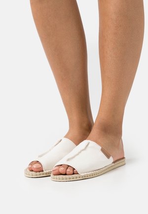 Hvide canvas slip-on sko med åben tå og flettet jutesål, med en struktureret overflade og et lille læderlabel.