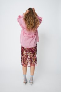 Pink striped shirt with ruffled sleeves paired with a sheer burgundy floral-embroidered skirt. Light blue ankle socks and heels complete the look.