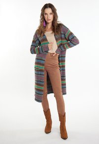 Pestrý pletený cardigan se stripe vzorem, dlouhými rukávy a volným střihem; v kombinaci s hnědými semišovými kalhotami a botami.