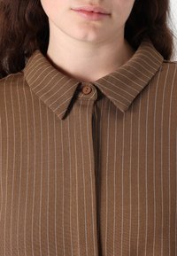 Brown striped shirt featuring a buttoned collar and subtle white pinstripes, made from a smooth fabric with a slight sheen.