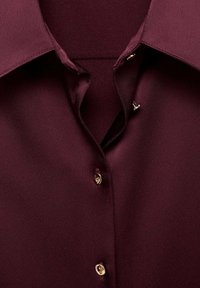Dark burgundy shirt collar with three visible small gold buttons on textured fabric, partially fastened with open top button.