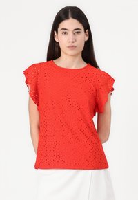 Haut rouge à manches courtes avec un motif en losange découpé et des manches volantes, fabriqué en tissu léger, avec un col rond.