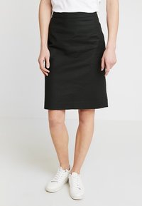 Svart knälång kjol i ett slätt tyg med hög midja, som har två sidofickor och rak skärning. Bärs med vita sneakers.