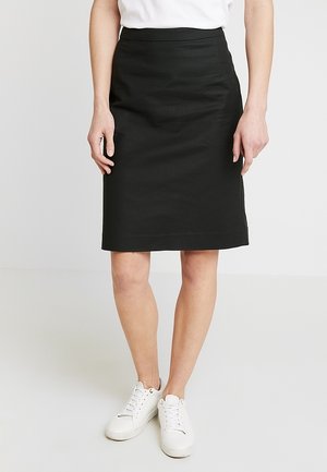 Jupe noire mi-longue en tissu lisse avec une taille moulante, dotée de deux poches latérales et d'une coupe droite. Portée avec des baskets blanches.