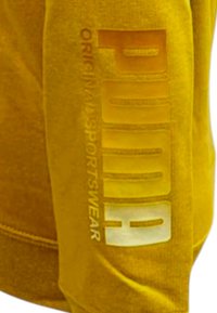 Felpa gialla caratterizzata da un tessuto testurizzato, taglio oversize e una stampa bianca prominente del logo del marchio e del testo sulla manica.