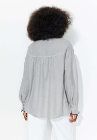 Chemise à rayures grises et blanches à manches longues avec une coupe décontractée, des poignets boutonnés et une couture arrière froncée. Tissu en coton texturé.