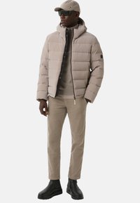 Beige puffer jacket with a hood and black zipper, paired with a light tan top and beige corduroy pants. Black ankle boots complete the look.