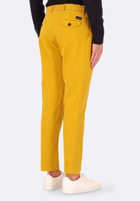 Pantaloni di cotone gialli con vestibilità slim e cintura elastica. Presentano tasche posteriori con chiusura a bottone e cuciture laterali per un tocco di dettaglio in più.