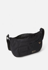 Black crossbody bag with adjustable strap, front pocket with flap, zippered main compartment, small ring detail, and Columbia logo patch.