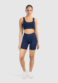 Námorně modrý sportovní set skládající se z užšího crop topu a šortek s vysokým pasem. Hladká tkanina s minimem švů, navržena pro pohodlí.