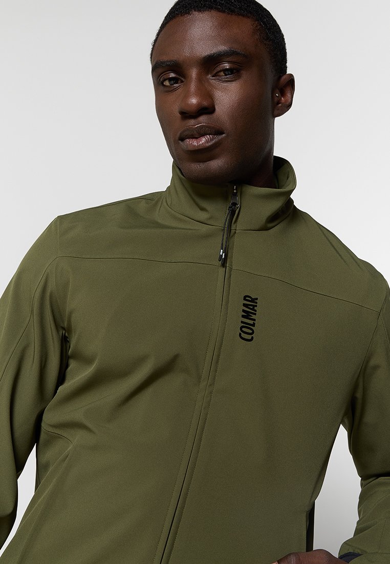 Giacca softshell verde oliva con colletto alto e zip completa, con un logo nero sulla parte frontale sinistra. Texture liscia e design aderente.