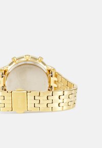 Goldfarbener Edelstahlchronographenuhr mit einem Armband aus verbundenen Gliedern, runder Gehäuserform und einer polierten Rückseite.