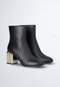 Czarne skórzane botki za kostkę o eleganckim kroju, ze złotym, kwadratowym obcasem z wypukłym logo. Gładka faktura, szpiczasty nosek.