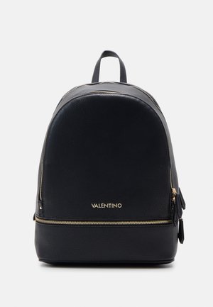 Sac à dos en cuir noir de forme arrondie, avec des zips dorés, un logo sur le devant et une poignée supérieure pour un transport facile. Détails de surface texturée visibles.