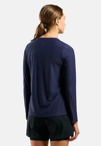 Marineblaues langärmliges Sportoberteil aus glattem Stoff, mit runder Halslinie und einem subtilen strukturierten Muster auf dem Rücken. Schwarze Shorts werden getragen.