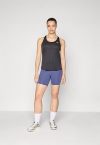 Débardeur de sport noir, short ajusté bleu marine, chaussettes blanches mi-mollet et chaussures de course grises. Présente un logo sur le débardeur et un design épuré.